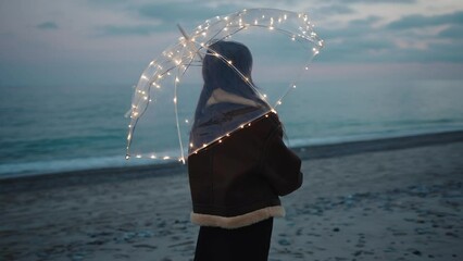 Wall Mural - Girl watching sunset with glowing magic umbrella on the beach