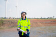 © narong - Pretty engineer or technician woman worker hold drawing paper and look at camera with smiling also stand in front of windmill cluster in workplace.
