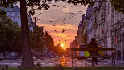 Wall Mural - Street with sunset in the Croatian capital Zagreb. People sitting on the bench near tree. Road traffic and tram rails