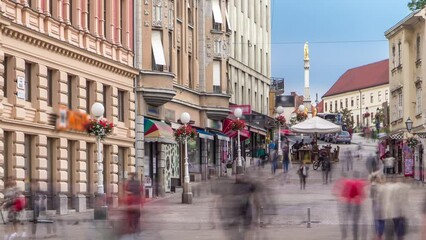 Wall Mural - Street with historic buildings in downtown and Holy Mary monument in front of the Cathedral on the background timelapse in Zagreb, Croatia. People walking around