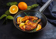 Traditional barbecue chicken drumsticks with orange slices served with herbs as close-up on a rustic metal frying pan