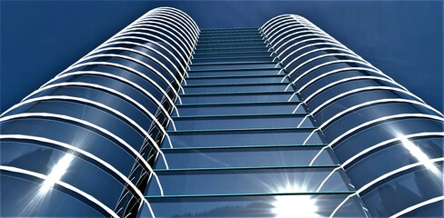 Wall Mural - Bright morning sun reflected in the glass facade of the contemporary office building with day illumination against the stunning blue sky. 3d rendering.