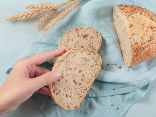 Wall Mural - Woman's hand holding a slice of fresh baked whole grain bread with flax seeds and sesame seeds