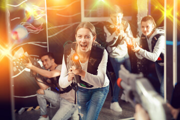 Canvas Print - Emotional girl with laser pistol playing laser tag with friends on dark labyrinth..