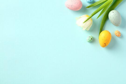 happy easter concept. colorful easter eggs with tulips on light blue background. flat lay, top view,
