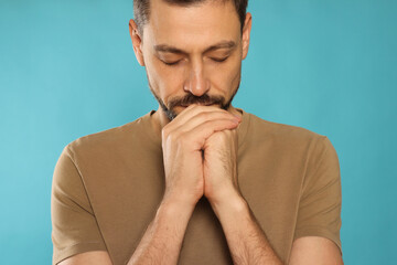 Wall Mural - Man with clasped hands praying on turquoise background