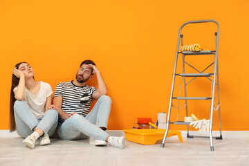 Canvas Print - Tired designers sitting on floor with painting equipment near freshly painted orange wall indoors