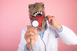 doctor with T Rex mask holding a stethoscope close-up on an isolated pink background. selective focus