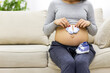 © Andrii - Cropped photo of pregnant woman sitting on the sofa with child clothes.