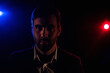© Andrii - Photo of man looking at camera on dark background with pink and blue lights.