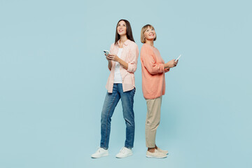 Wall Mural - Full body fun happy elder parent mom with young adult daughter two women together wear casual clothes hold in hand mobile cell phone look overhead isolated on plain blue background Family day concept