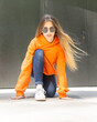 © Cavan Images - City portrait of positive young female wearing casual clothes orange. Grey background