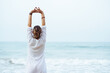 © Cavan Images - Woman with her back and white dress doing stretching on the beach.