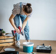 © olezzo - A young woman in her 30s making repairs in the house stirring the paint for the walls. House renovation and renovation project concept