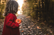 Little Girl Outside In A Fall Forest Holds A Tiny Pumpkin In Her Hand