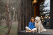 © rh2010 - Young woman sits with her dog on porch of a wooden house in pine forest, enjoying nature while resting in cottage at countryside