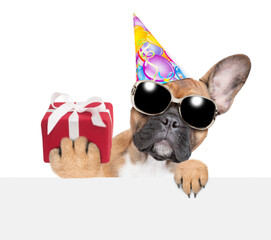 Poster - French Bulldog puppy holds gift box and looks above empty white banner. isolated on white background