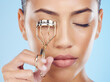 Cosmetics, routine and woman with an eyelash curler isolated on a blue background in a studio. Skincare, beauty and face of model with a metal product for lashes, makeup and mascara on a backdrop