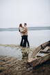 © Anhelina  - a man and a woman stand on the shore of a lake, cold foggy weather. A wooden boat. holding a woman's hand, a love story. beige sweaters. romantic photos against the background of a foggy lake