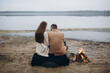 © Anhelina  - foggy evening by the lake, a bonfire is burning. a man and a woman are sitting on the shore of a lake near a bonfire. beige men's coat. love story photo shoot in cloudy foggy weather