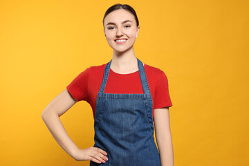 Wall Mural - Beautiful young woman in clean denim apron on orange background