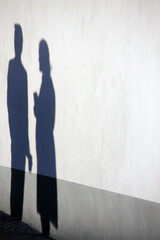 Shadow of two people on the wall, one holding a glass and the other holding her bag in her arms.