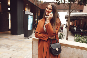 Cute brunette woman in brown coat talking on the phone in the city