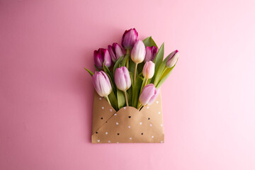 Pink and purple tulips in a paper envelope on a pink background copy space