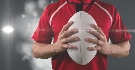 Poster - Mid section of caucasian male rugby player holding rugby ball against light spot on grey background