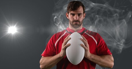 Wall Mural - Portrait of caucasian male rugby player holding ball against smoke and light spot on grey background