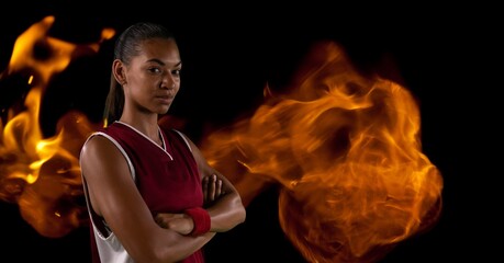 Wall Mural - Composition of female basketball player with arms crossed over flames on black background