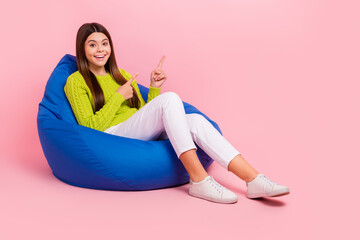 Sticker - Full length photo of cute young girl sitting bean bag excited point empty space wear trendy green outfit isolated on pink color background