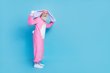 Sticker - Full length photo of funky positive good mood senior man dressed pink rabbit costume arms hold ears isolated on blue color background