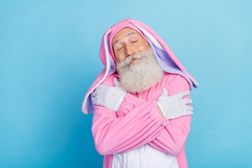 Poster - Portrait of cheerful positive man dressed pink rabbit costume cuddle himself enjoy comfort sleepwear isolated on blue color background