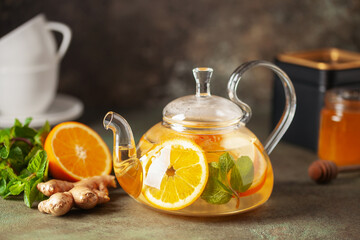 Wall Mural - Glass teapot with hot citrus tea from oranges, lemons, apples, ginger and mint. Healthy drink on dark background