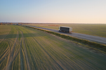 Poster - Aerial view of semi-truck with cargo trailer driving on highway hauling goods in evening. Delivery transportation and logistics concept