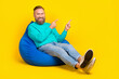 © deagreez - Full size photo of handsome granddad sitting beanbag point empty space dressed stylish cyan garment isolated on yellow color background