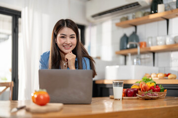 Wall Mural - Beautiful young asian woman working on laptop computer while sitting at the kitchen room background.