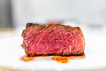 Wall Mural - Cooked rare blue red raw strip steak cut half macro closeup side view on white plate on table with blurry bokeh background and vein