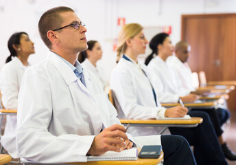 Wall Mural - Portrait of male doctor attentively listening to lecture with colleagues at medical conference