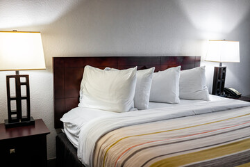 Bedroom closeup of four white pillows with sheets on mattress bed headboard in modern hotel with empty room and illuminated lit lamps lights and nobody