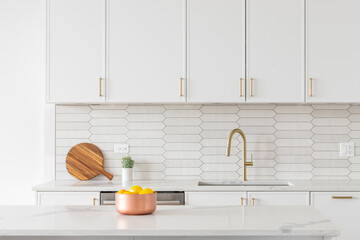 Wall Mural - A beautiful kitchen faucet detail with white cabinets, a gold faucet, white marble countertops, and a brown picket ceramic tile backsplash.