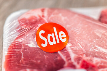 Macro closeup of sale sticker label sign on packaged raw pink red pork chops for cooking