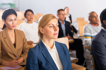 Canvas Print - Portrait of young adult female attentively listening to motivation lecture with colleagues at conference