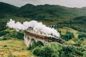 A steam train crossing the Glenfinnan viaduct in the Scottish Highlands made famous by the Harry Potter movies. The Jacobite steam train crossing the bridge with steam in Scotland United Kingdom