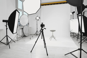 Canvas Print - Tripod with camera, bar stool and professional lighting equipment in modern photo studio