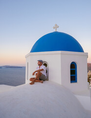 Wall Mural - Young men watching the sunrise in Santorini Greece, man on vacation at the Greek village Oia with whitewashed house and churches.