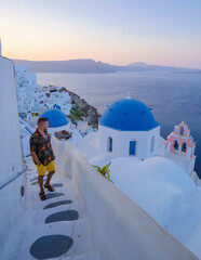 Wall Mural - Young men watching the sunrise in Santorini Greece, man on vacation at the Greek village Oia with whitewashed house and churches.