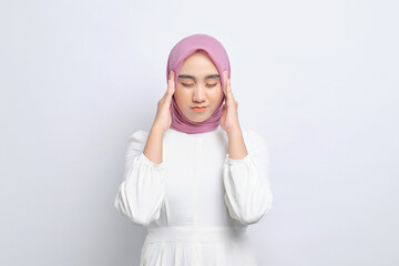 Wall Mural - Stressed young Asian Muslim woman touching her temples and having headache isolated over white background
