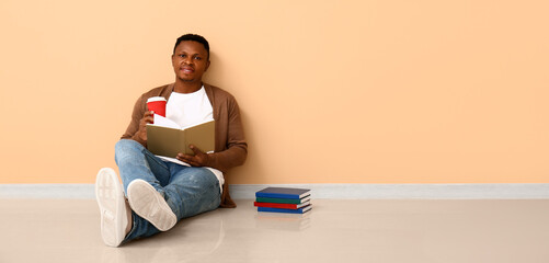 Wall Mural - African-American man reading book near beige wall. Banner for design